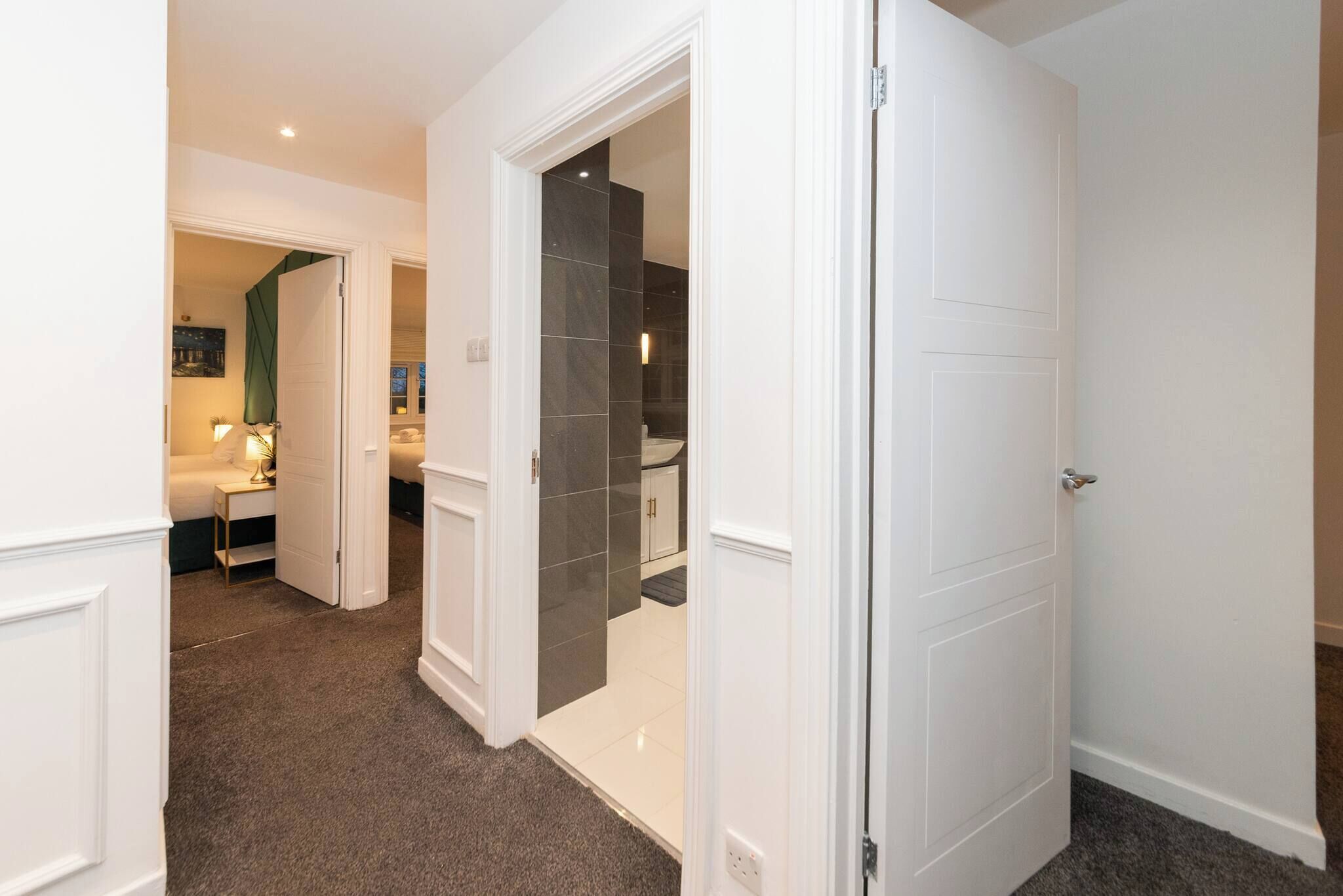 A hallway with a carpeted floor leading to a bedroom with a bed and a nightstand.