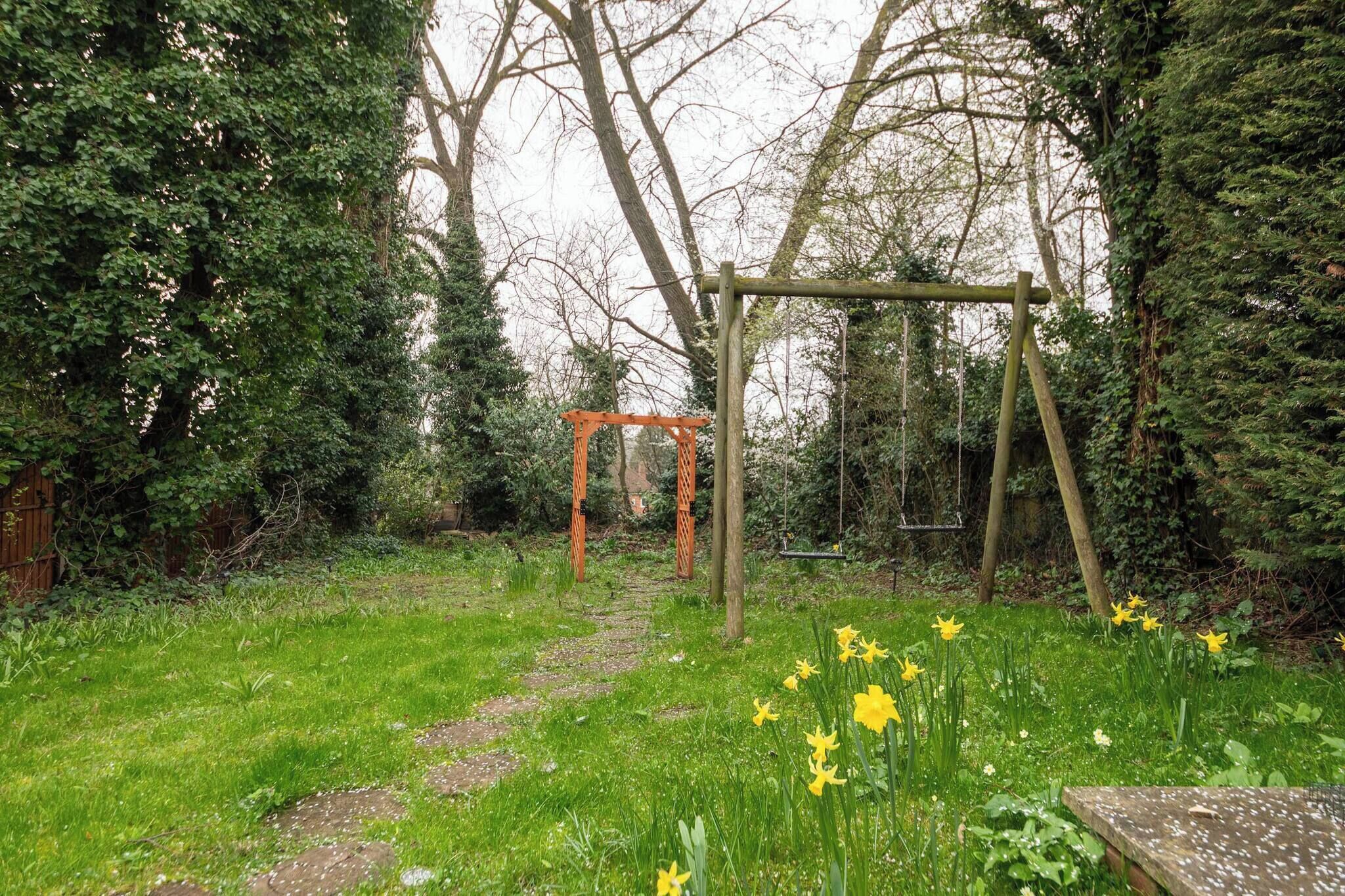 A garden with a wooden swing set, a path, and yellow daffodils.