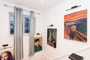 Ein Flur mit Bildern an den Wänden, einem Fenster mit Vorhängen und einer Tür am Ende.