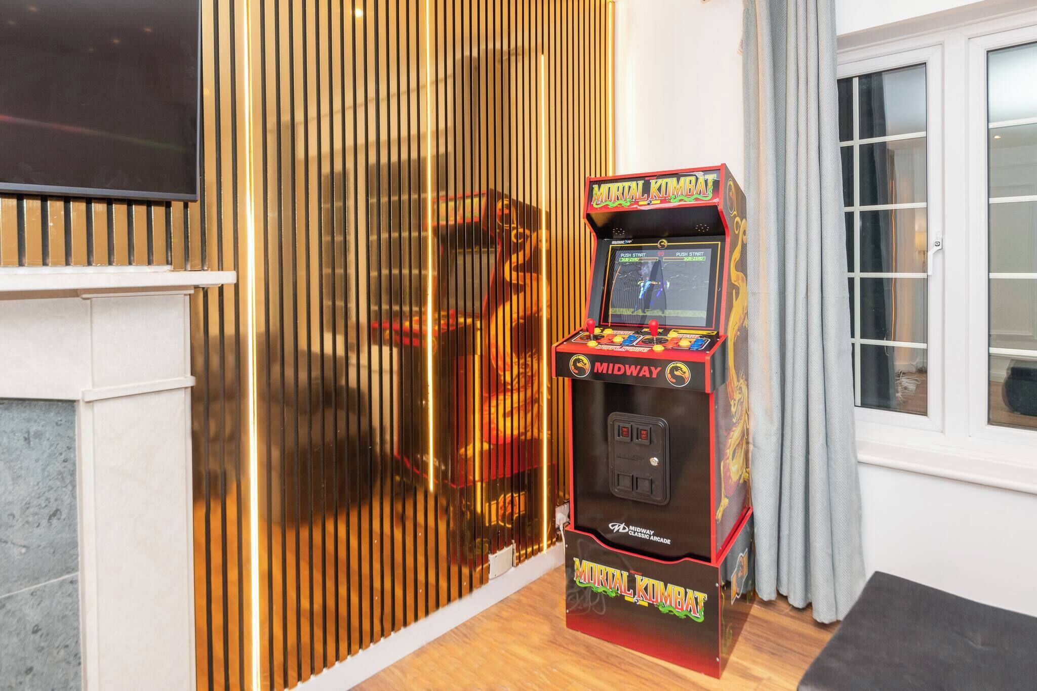 Máquina de videojuegos Midway con un diseño clásico, ubicada en un interior cerca de una ventana con cortinas.