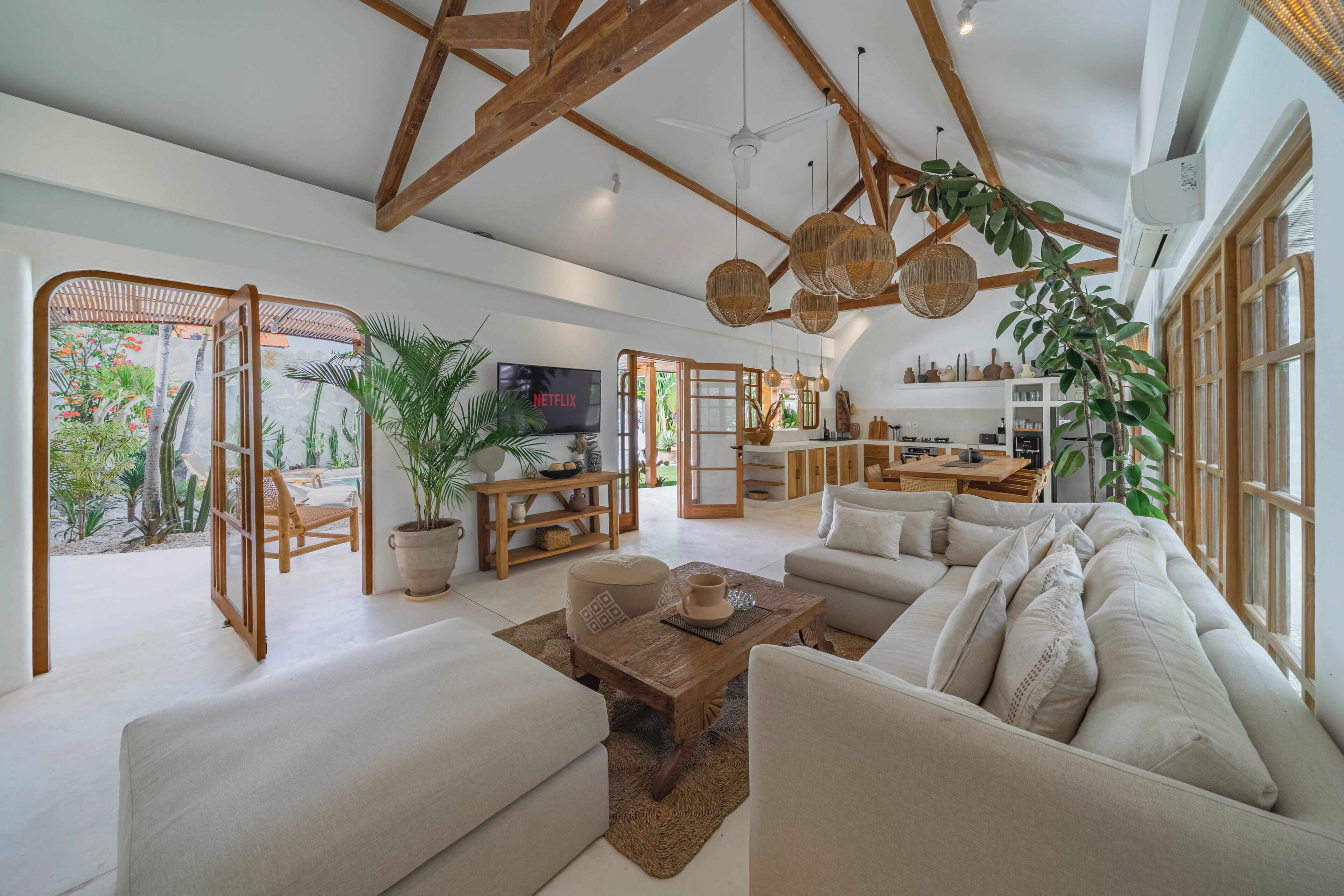 A spacious living area with a large sofa, a coffee table, and a television. There is a kitchen area with cabinets and a dining table.