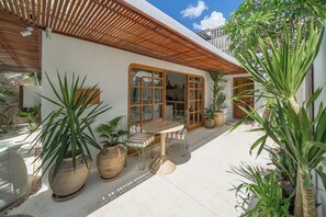 Eine Terrasse mit Tisch und Stühlen, umgeben von großen Kübelpflanzen.