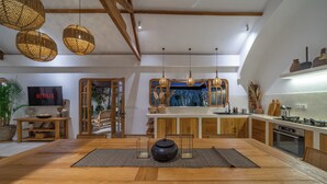 Eine moderne Küche mit Holzausstattung, ein Essbereich mit großem Tisch und ein Fernseher im Hintergrund.