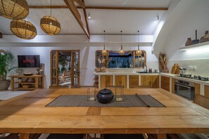 Eine moderne Küche mit Holzausstattung, ein Essbereich mit großem Tisch und ein Fernseher im Hintergrund.