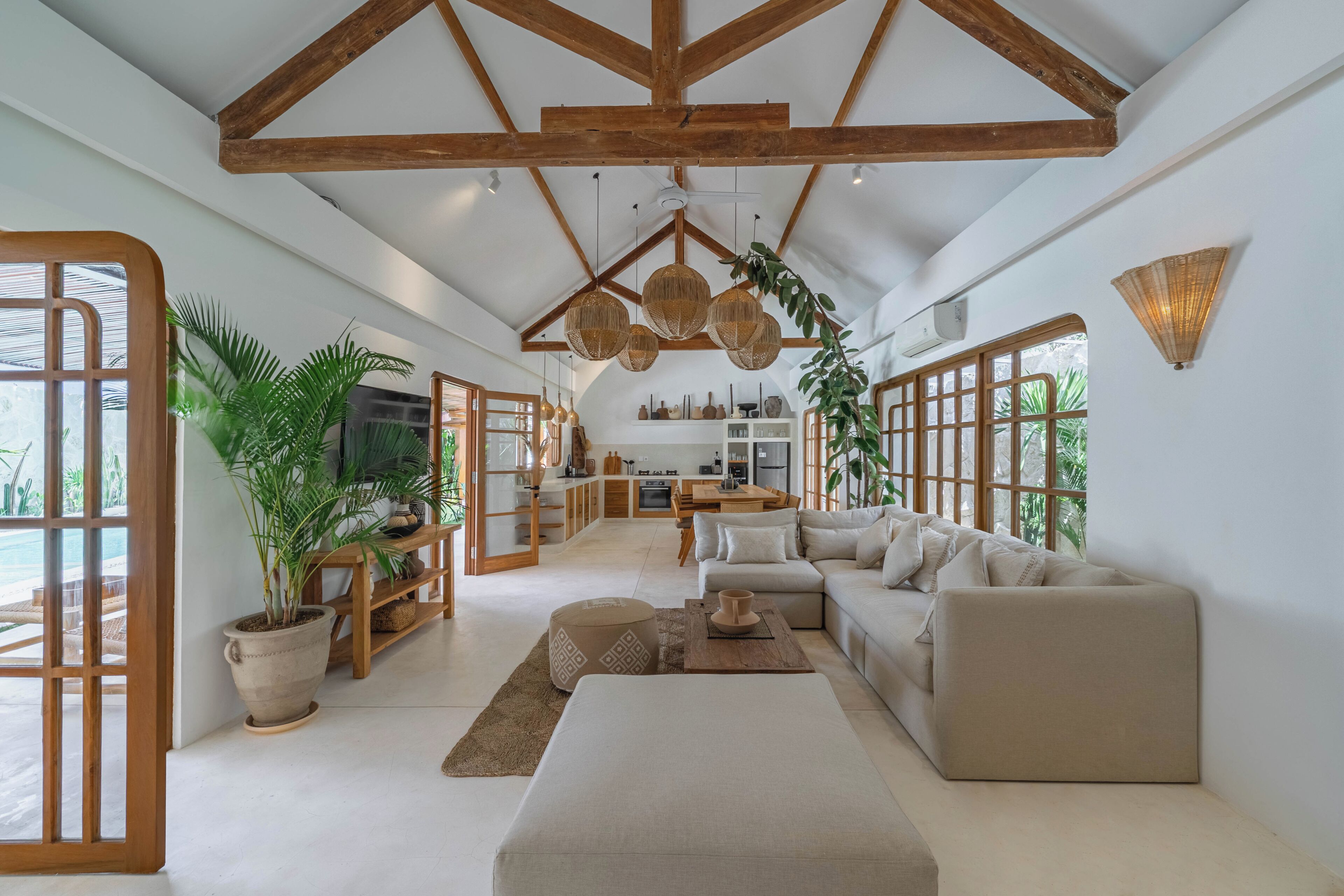A spacious living area with a high ceiling, wooden beams, a sofa set, a coffee table, and potted plants.