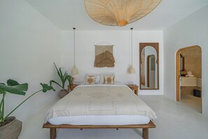 Ein Schlafzimmer mit einem Bett, Nachttischen, einer Pendelleuchte, einem an der Wand befestigten Spiegel und einer Tür zu einem Badezimmer.