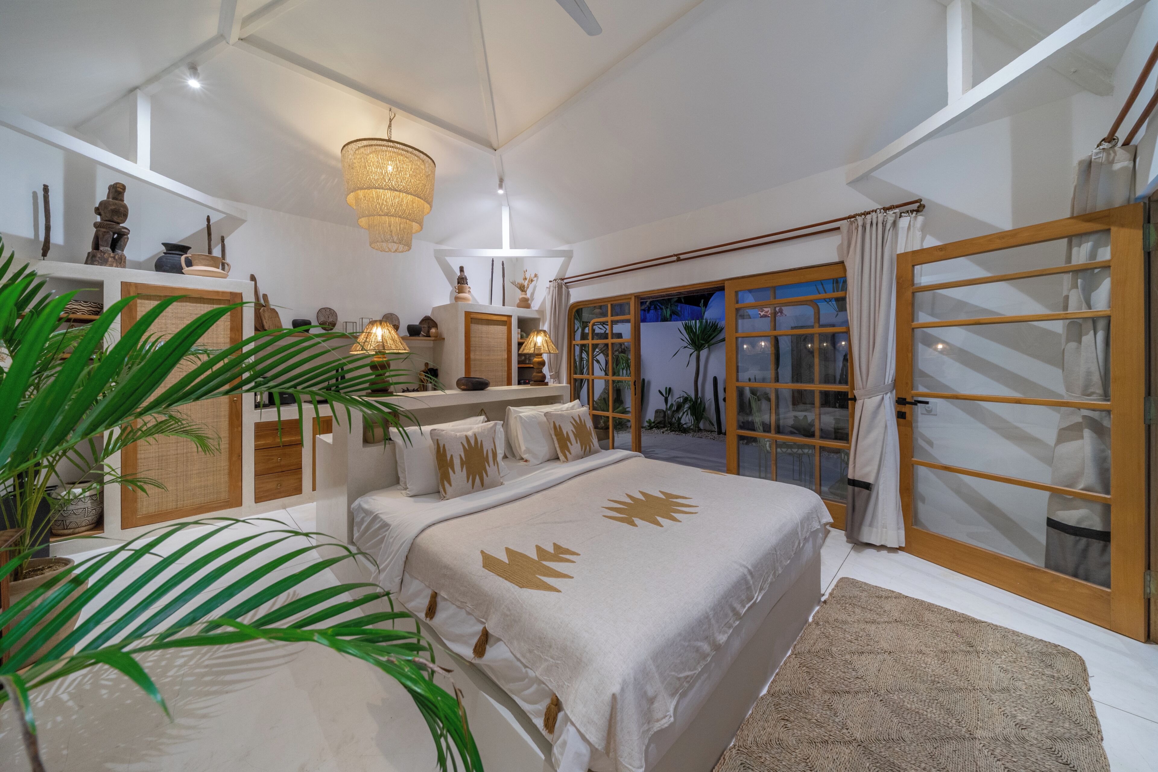 A bedroom with a large bed, a chandelier, a view of the outdoors, and a sliding glass door.
