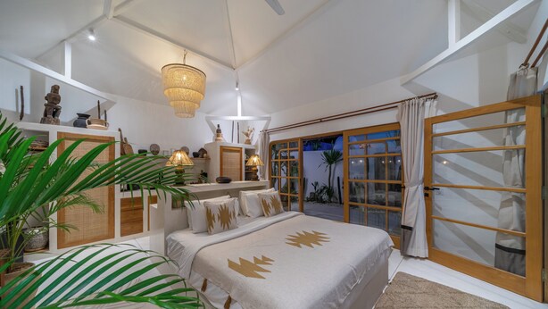 Ein Schlafzimmer mit einem großen Bett, einem Kronleuchter, Blick ins Freie und einer Schiebetür.