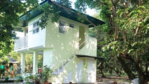 A two-story building with a balcony, surrounded by trees and gravel. - Fully furnished house, a café & pool in a forest! (Naujan)