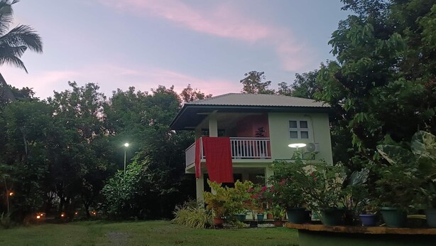 Een huis met balkon, omringd door weelderig groen en een rieten dakgebouw.
