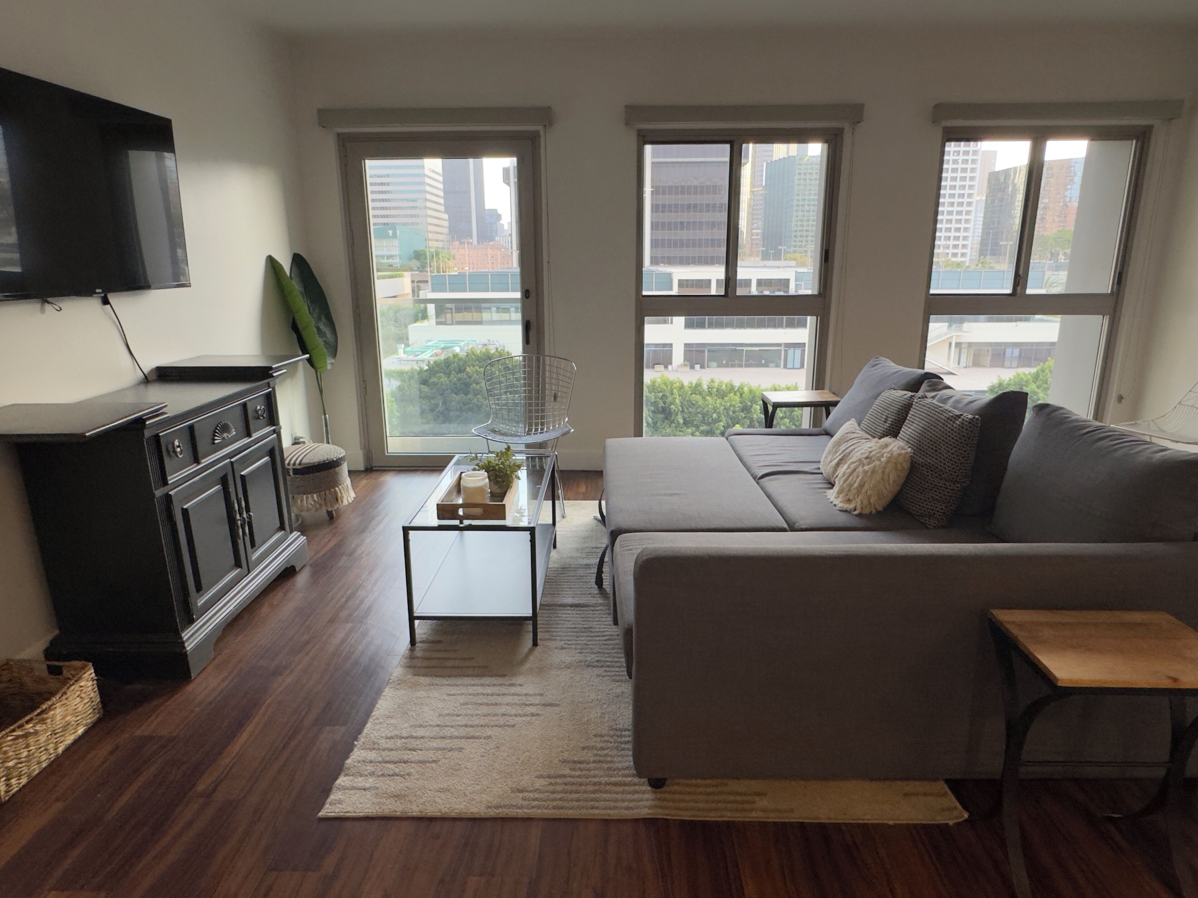 A modern living room with a sofa, a coffee table, a TV, and large windows offering a city view.