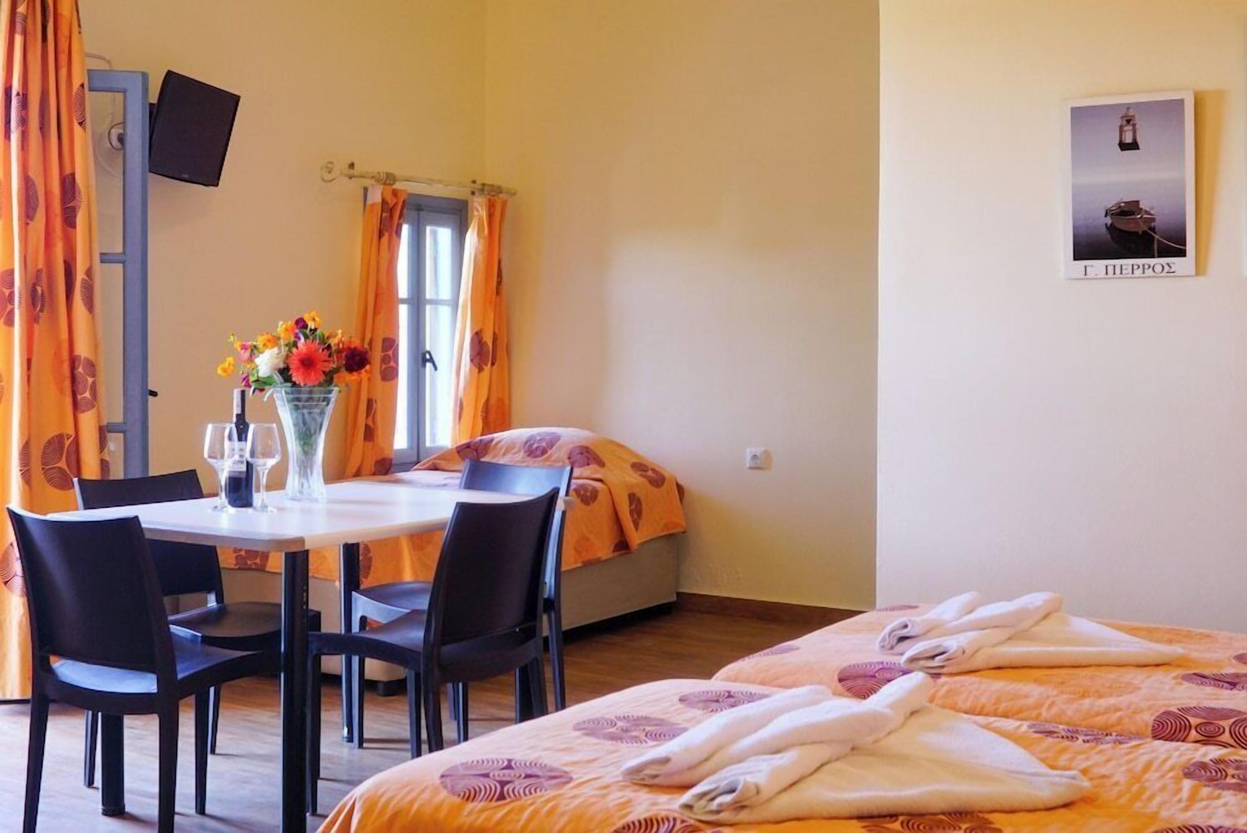 Una habitación de hotel con cama, una mesa y sillas, un florero con flores y un cuadro en la pared.