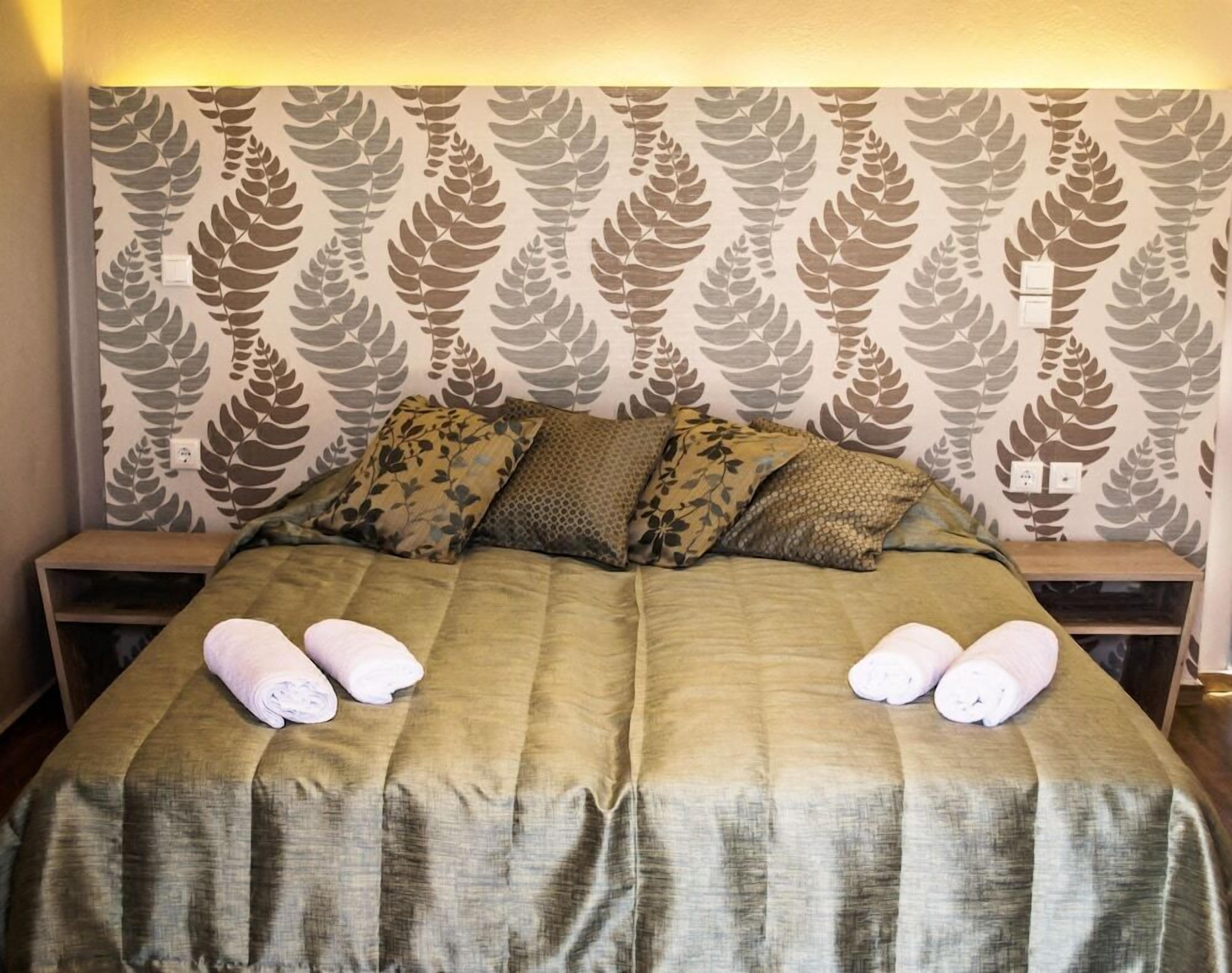 A bed with a patterned headboard, two bedside tables, and towels on the bed.