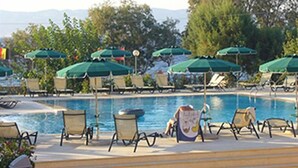 A poolside area with lounge chairs and umbrellas, a clear sky, and trees in the background. - Lassia Hotel (Lesvos)