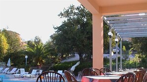 A poolside area with lounge chairs and tables, surrounded by greenery. - Lassia Hotel (Lesvos)