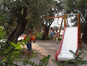 A playground with a slide and swings, surrounded by trees. - Lassia Hotel (Lesvos)