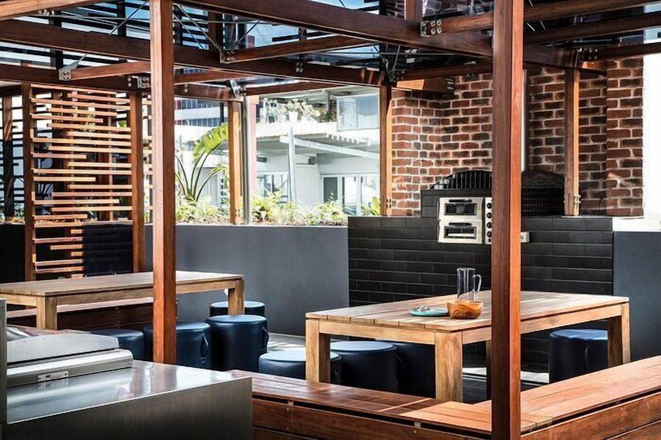 An outdoor seating area with wooden tables and benches, a brick wall, and a grill.