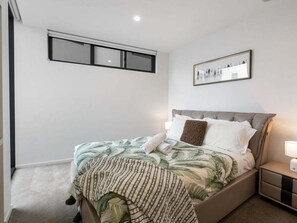 Ein Schlafzimmer mit einem Bett, einem Nachttisch, einem gerahmten Bild an der Wand und einem Fenster mit Jalousien.