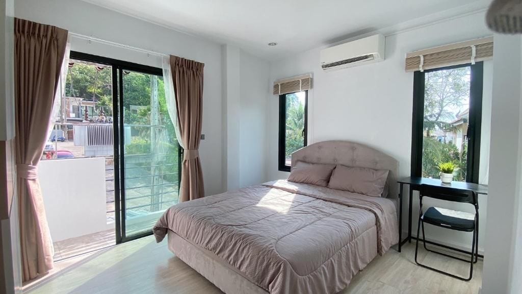 A bedroom with a bed, a desk, and a chair. There are curtains on the windows, and an air conditioning unit is mounted on the wall.