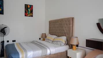 Una camera da letto ordinata con un letto, lampade sui comodini, una ventola e un quadro appeso al muro.