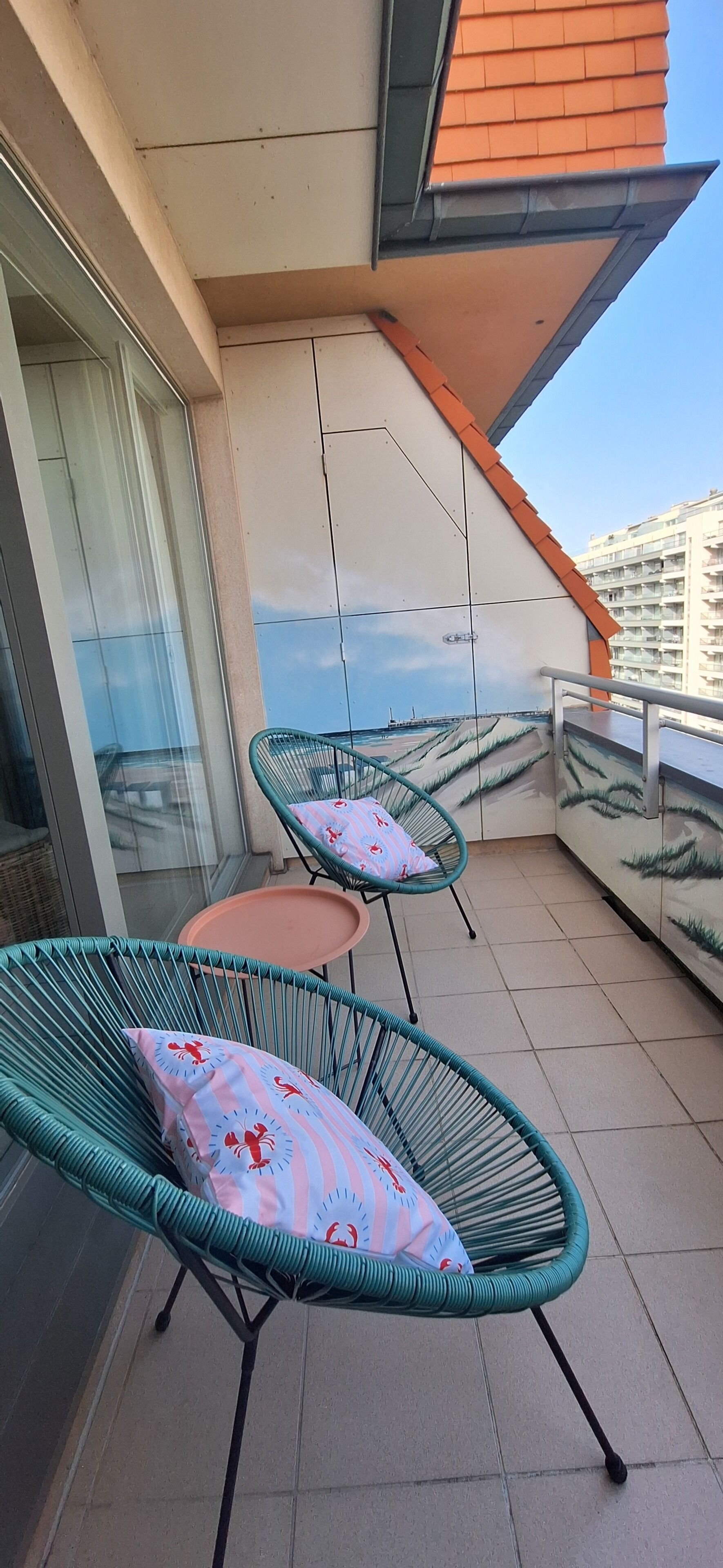 A balcony with two green wire-framed chairs and a small round table, each with a cushion.