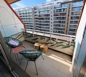 Ein Balkon mit zwei Stühlen, einem kleinen Tisch und einer Wand mit dekorativem Pflanzenmuster.