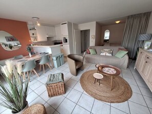 Ein modernes Wohnzimmer mit einer Couch, einem Essbereich mit Stühlen, einer Küche mit Schränken und einem großen Spiegel an der Wand.