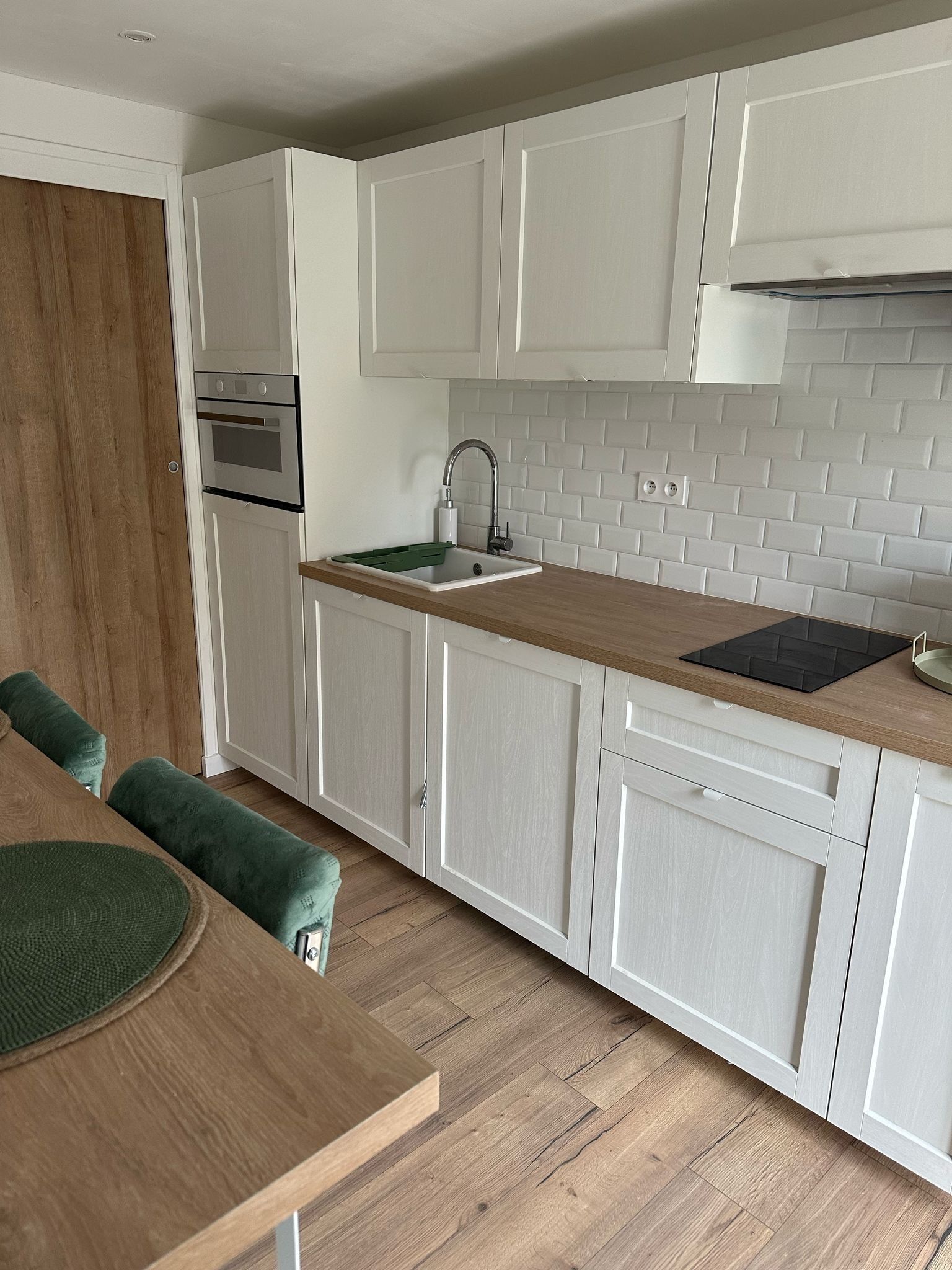 A modern kitchen with white cabinetry, a wooden countertop, a built-in oven, and a sink.