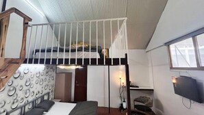 A room with a bunk bed, a desk, a chair, a television, and a window.