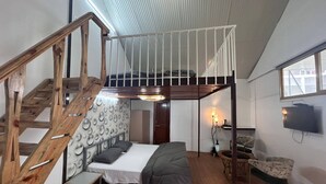A room with a bunk bed, a wooden staircase, a small table, a chair, and a television mounted on the wall.