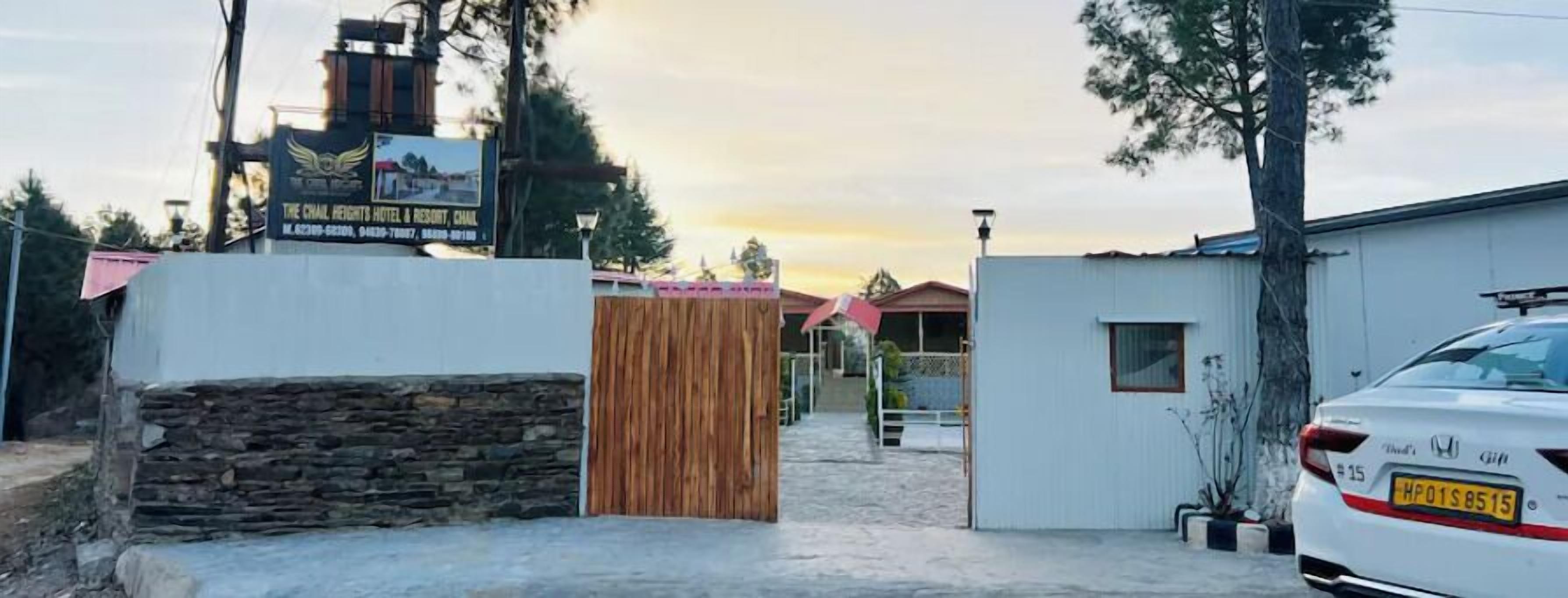 A gated entrance to a property with a signboard, a white car parked on the right, and a stone wall on the left.