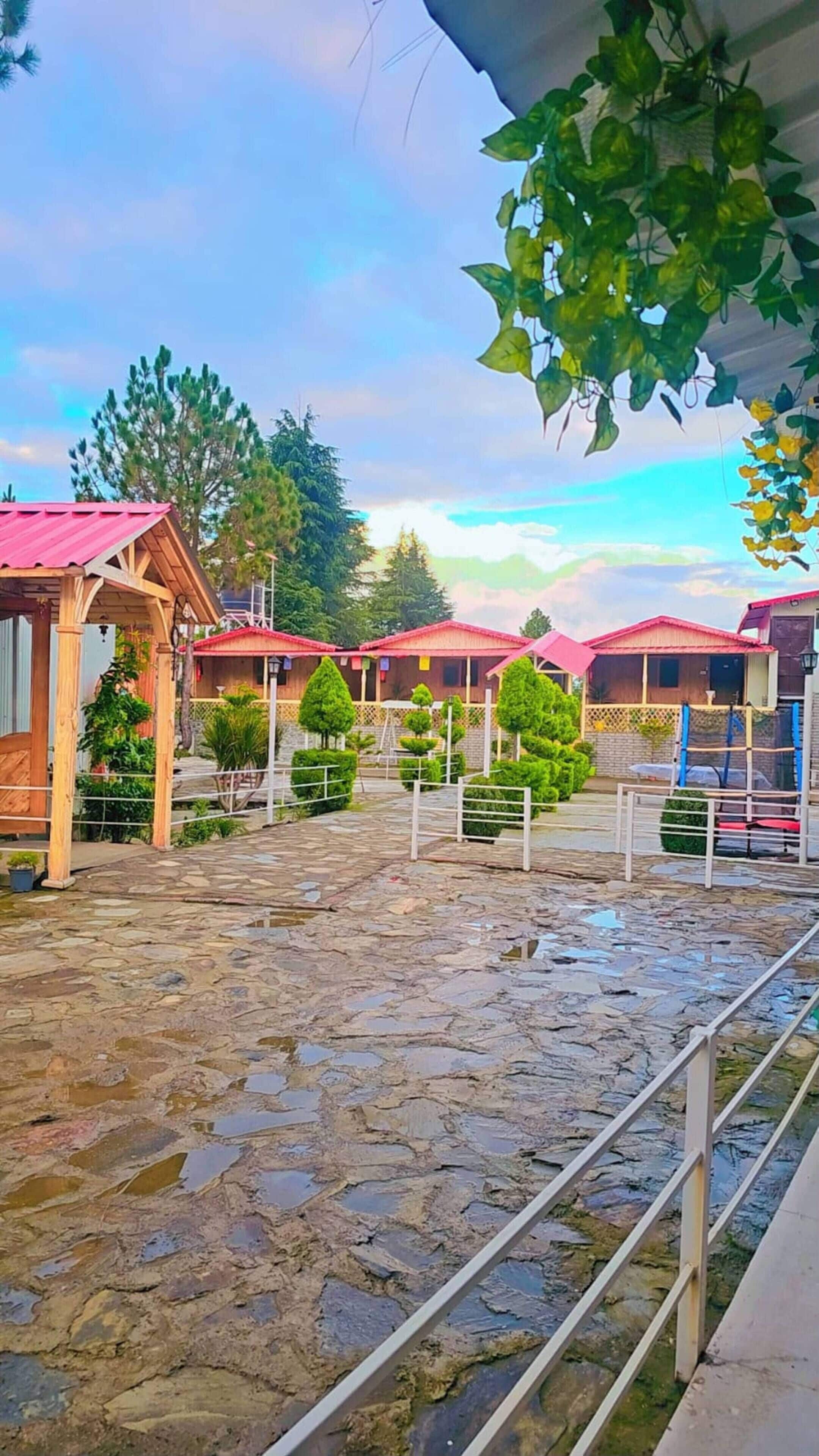 A stable with a red roof, surrounded by trees and a stone floor.