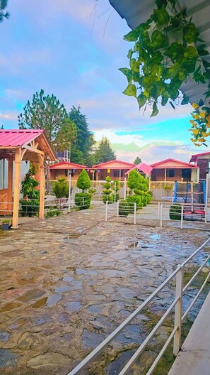 A stable with a red roof, surrounded by trees and a stone floor.