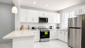 Una cocina moderna con armarios blancos, un refrigerador de acero inoxidable, horno empotrado y microondas.