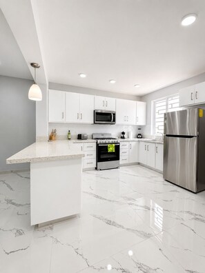 A modern kitchen with white cabinetry, a stainless steel refrigerator, a built-in oven, and a microwave. - 2-bedroom house in welcoming Tequila with AC for relaxing stays (Tequila)