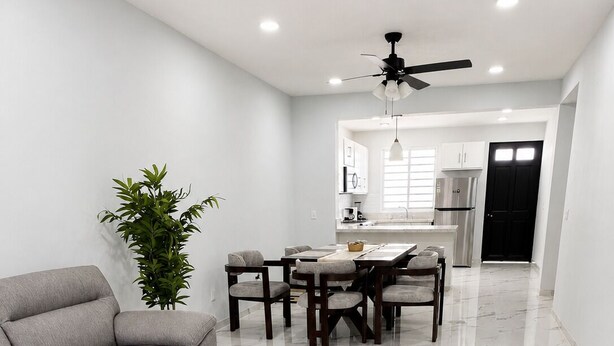 Una sala moderna con sofá, mesa de comedor, sillas y ventilador de techo.