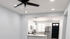 Una cocina moderna con armarios blancos, un refrigerador de acero inoxidable y un comedor con piso de mármol y una mesa de madera oscura.