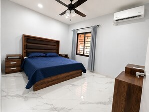 A bedroom with a bed, nightstands, a ceiling fan, an air conditioning unit, a window with curtains, and a wooden cabinet. - 2-bedroom house in welcoming Tequila with AC for relaxing stays (Tequila)