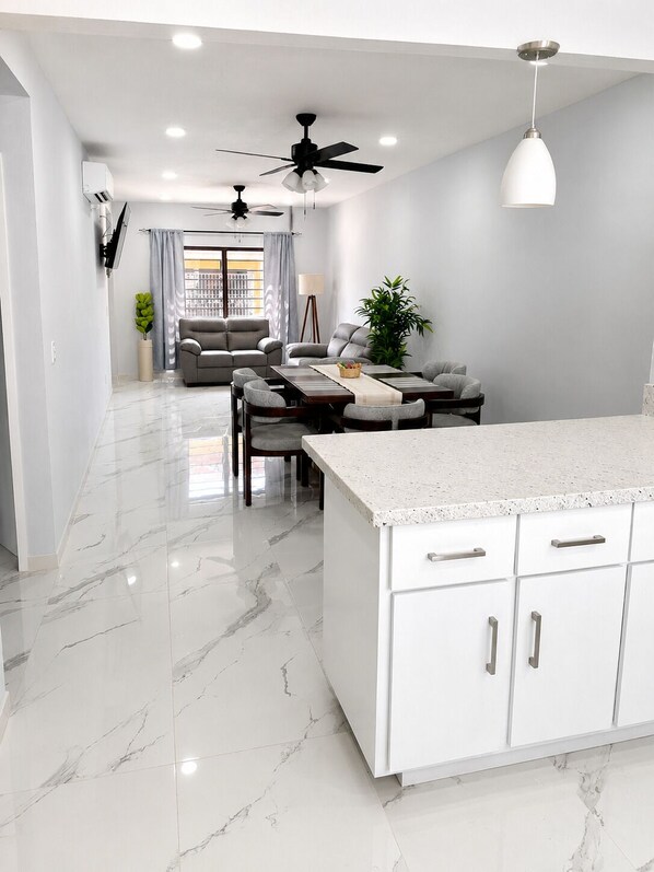 A modern kitchen with white cabinetry, a marble countertop, and a ceiling fan.
