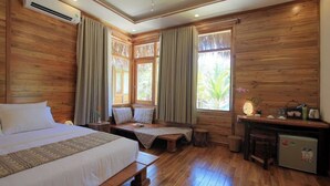 Quarto com piso de madeira, uma cama, um banco, uma escrivaninha e uma pequena geladeira.