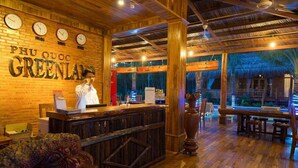 Interior de restaurante com balcão de madeira, um cozinheiro e vista tropical.