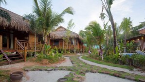 Um resort tropical com cabanas de teto de palha, um caminho de pedras e vegetação exuberante.