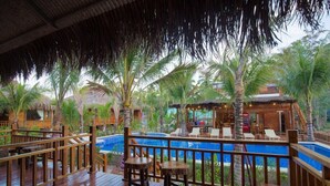 Um deck de madeira com piscina, cadeiras de descanso e área de bar.