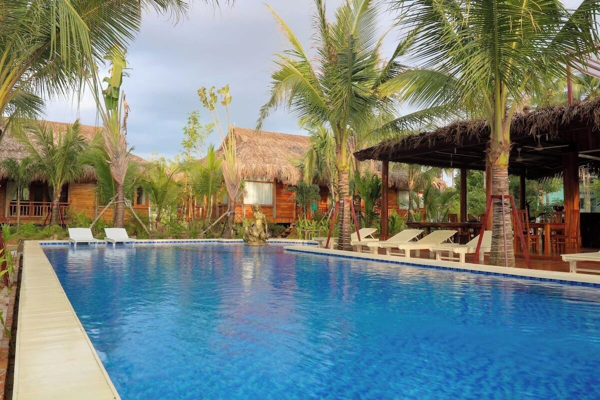 A swimming pool with lounge chairs, palm trees, and thatched-roof huts.