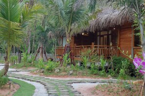 A wooden cabin with a thatched roof surrounded by lush greenery and a stone pathway. - Phu Quoc Green Land Resort (Phu Quoc)