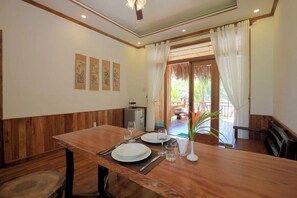 A dining area with a wooden table set for two, a small refrigerator, and a plant. - Phu Quoc Green Land Resort (Phu Quoc)
