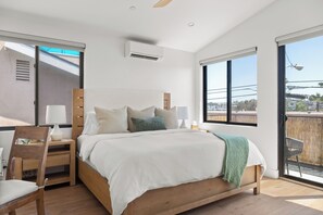 Ein Schlafzimmer mit einem großen Bett, einem hölzernen Kopfteil, Nachttischen mit Lampen, einem Ausblick durch ein großes Fenster und einer Klimaanlage.