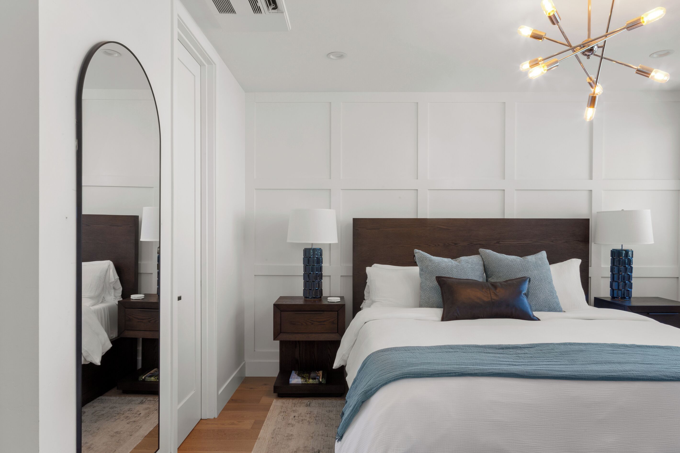 Quarto com uma cama grande, duas mesas de cabeceira, um espelho e um lustre moderno.