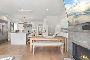 Et moderne køkken med en central ø, et spiseområde med bænk og en pejs.