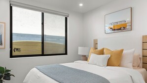 A bedroom with a large window, a bed with multiple pillows, a bedside table with a lamp, and a framed picture on the wall. - NEW: Fun on 4th Encinitas (Aug 2026) rooftop fire pit (Encinitas)